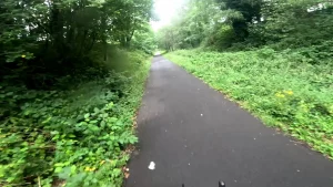 Cyling down a shared pedestrian/cycling pathway through a green space on a slightly rainy day.