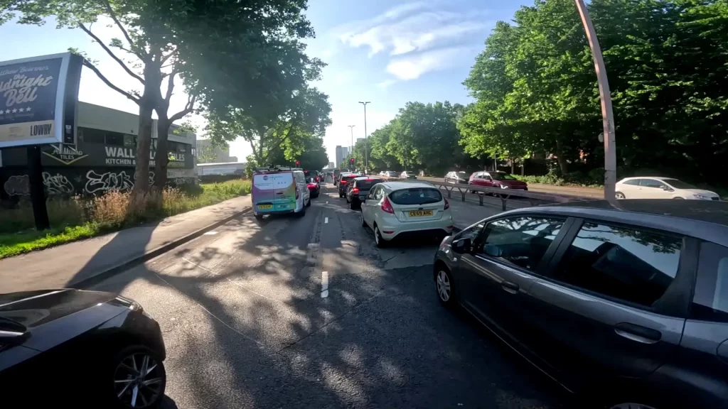 A cyclist filtering through slow-moving traffic on a busy road during a morning commute, avoiding what could be a common beginner mistake of choosing speed over a calmer route.