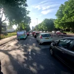 A cyclist filtering through slow-moving traffic on a busy road during a morning commute, avoiding what could be a common beginner mistake of choosing speed over a calmer route.