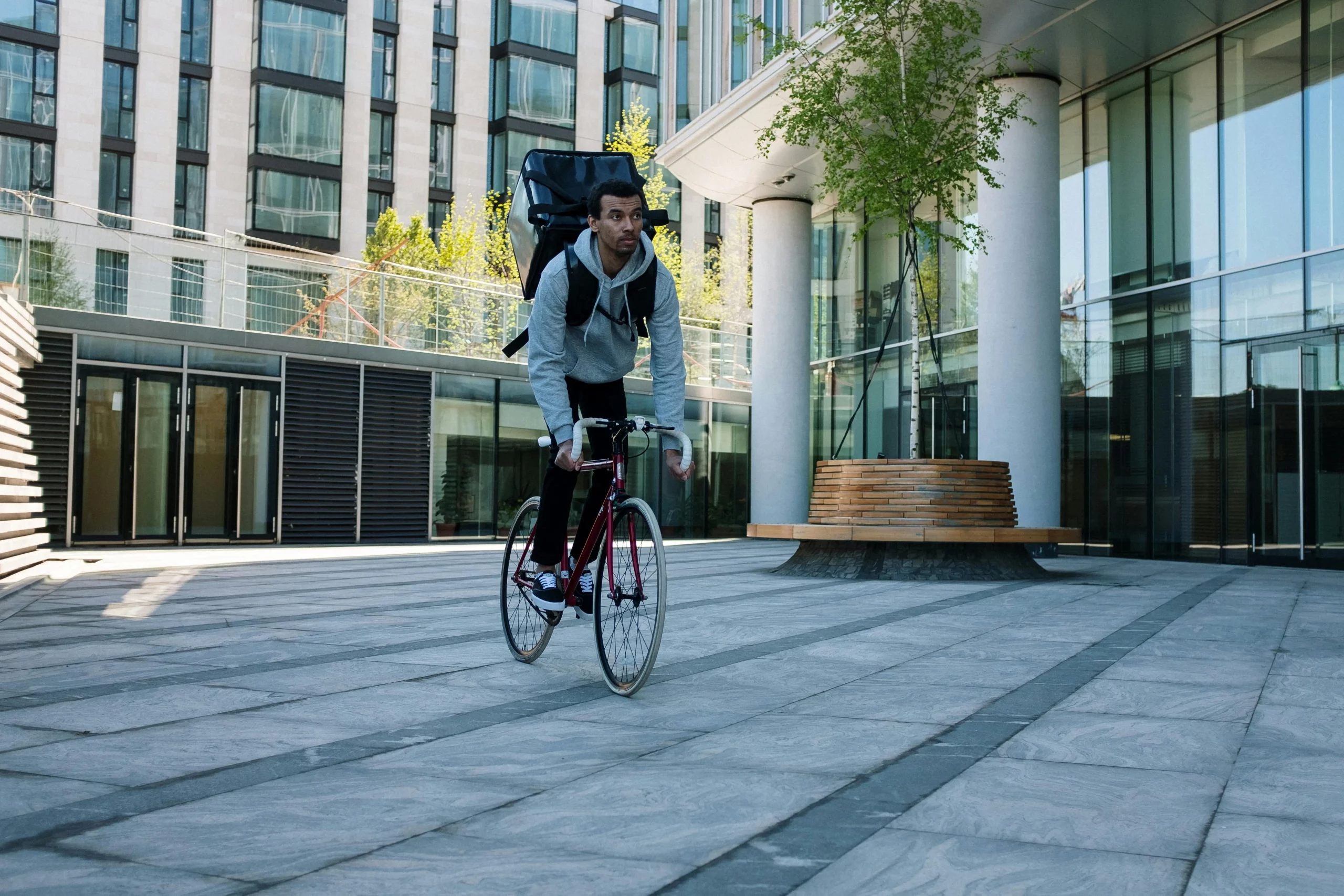 Image shows a delivery cyclist with a take out food backpack riding through and empty plaza.