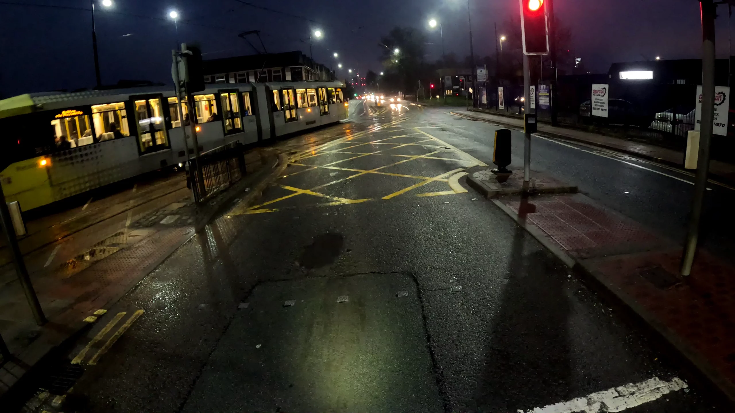 A cyclist sat at a red traffic light on a rainy morning, while a tram passes in front of them.
