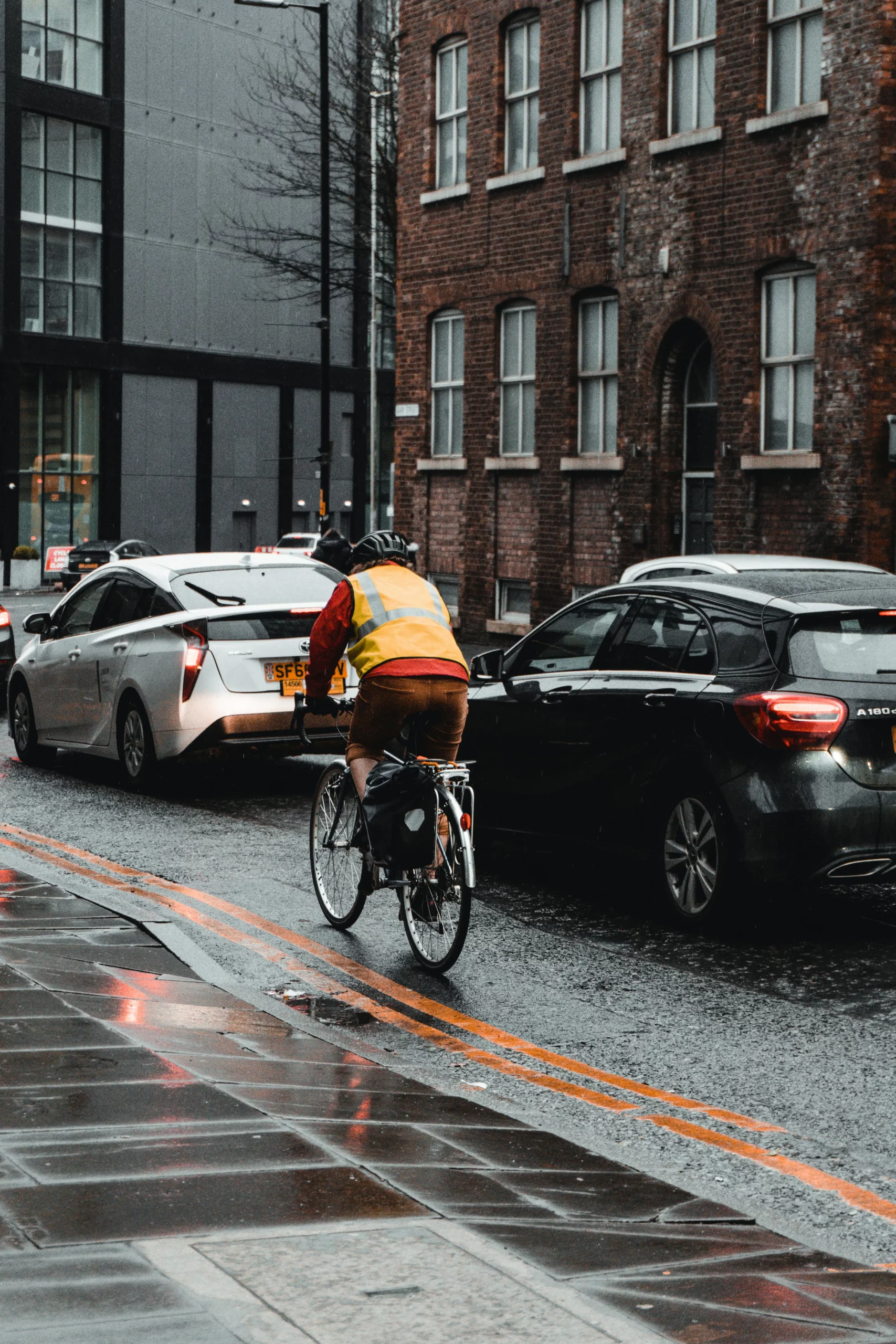 A cyclist riding down a wet road on a rainy day past traffic