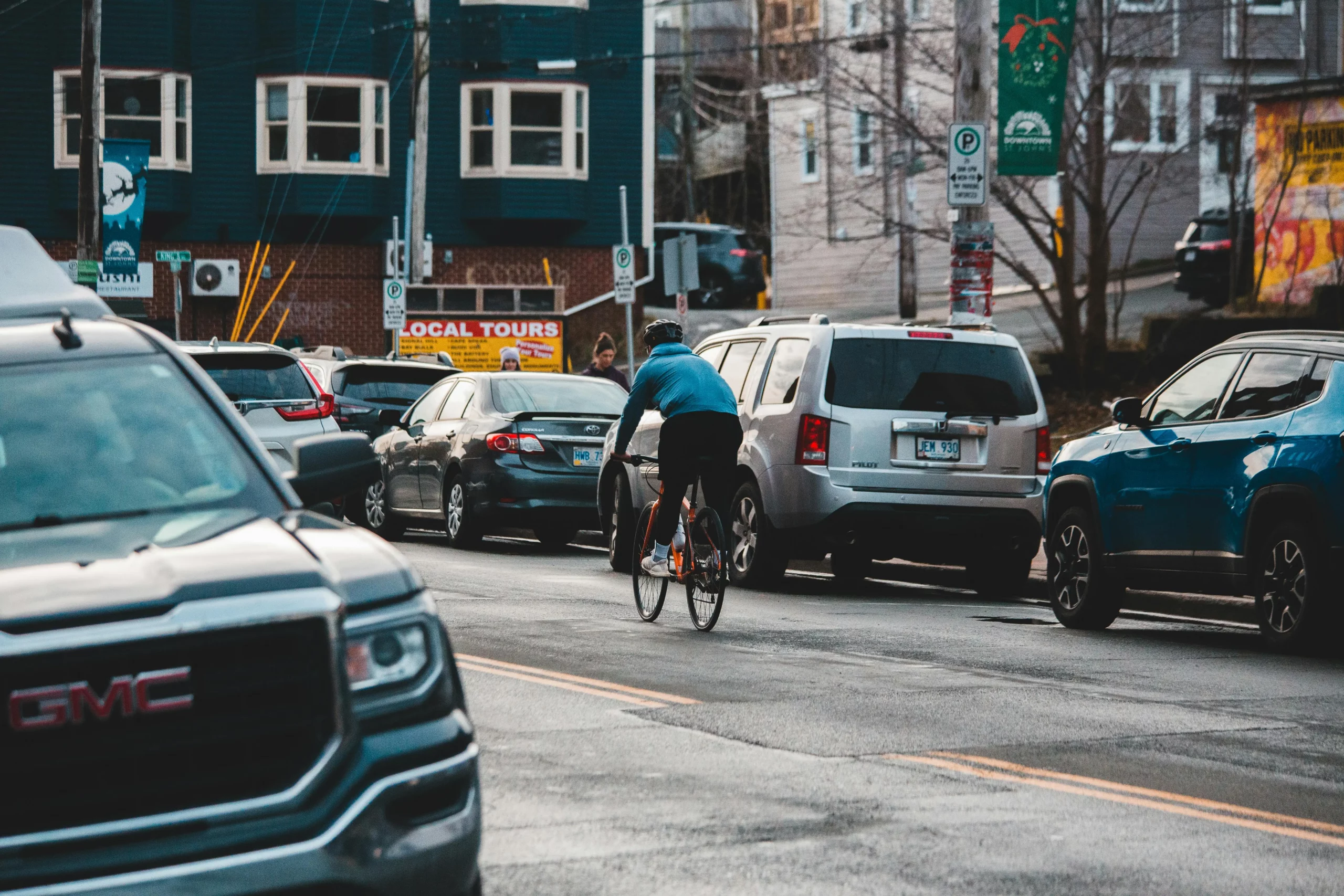 Cyclist taking centre lane on busy road with lots of parked cars