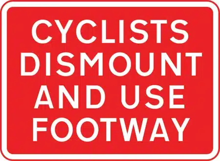 A red informational sign telling cyclists to dismount and use footway